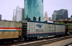 A gray boxcar with blue stripes at top and bottom. A dotted red stripe is above the lower blue stripe.