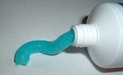 A photo of the end of a tube of toothpaste that has a manufactured opening with blue toothpaste extending out