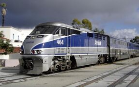 A passenger train with bilevel passenger cars painted in gray and blue stripes. The blue stripe on each side tapers to a point on the nose of the locomotive.