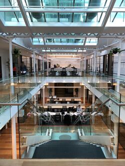 A coworking space on two levels with stairs and people working together. Underneath a big glass atrium
