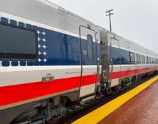Gray rail passenger cars with a thick red sill stripe and a thick blue window stripe flanked by thinner white stripes