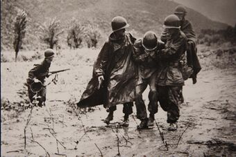 In this undated file photo, U.S. Army Capt. Emil Kapaun, right, a chaplain with the 3rd Battalion, 8th Cavalry Regiment, 1st Cavalry Division, helps a Soldier carry an exhausted troop off the battlefield 130311-A-CP123-001.jpg