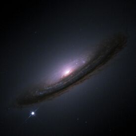 A dusty spiral galaxy seen close to edge-on against a black background, with a bright point of white at lower left