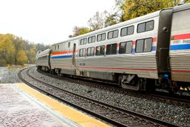A stainless steel passenger rail car with red, white, and blue stripes of equal width on the side