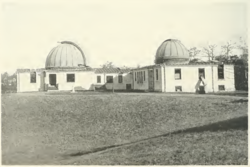 black and white image of a white building topped by two closed telescope domes