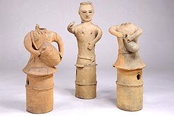 Three plain clay figures, featuring long, skirt-like columnar bases. The outer two figures are depicted playing drums. Only one figure, in the middle, has a head.