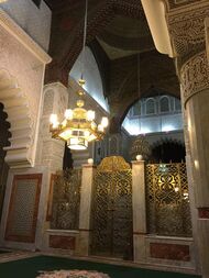 Interior of the mausoleum of Ahmad al-Tijani showing chandeliers, a decorated gate, and archways