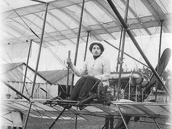 A woman sits at the controls of an early aeroplane