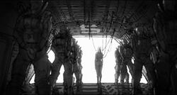Black-and-white drawing of a small woman, connected to wires, in front of wide open door, with two queues of large, suited soldiers in "at attention" pose flanking her either sides