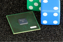 A photograph of the chip next to a pair of dice for size comparison
