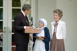 US President Ronald Regan and Nancy Reagan with Mother Teresa, standing at a microphone