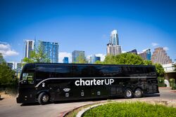 A black CharterUP motorcoach parked in front of the Austin skyline.