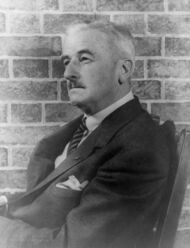 Faulkner is pictured in a chair before a brick well. He looks to the left.