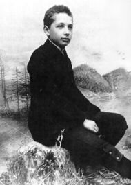 Studio photo of a boy seated in a relaxed posture and wearing a suit, posed in front of a backdrop of scenery.