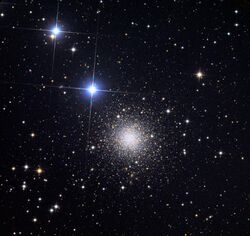 A round cluster of tiny distant stars with two bright bluish stars to the upper left