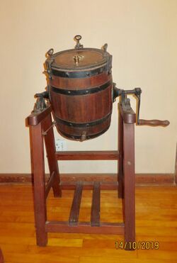 Barrel shaped oak container, rotating on pine framework or stand. Used in a farm environment to manually agitate cream to produce butter and buttermilk, the byproduct of butter production.