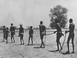 Black and white photo of children leading a line of adults across a dry landscape