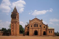 Photograph depicting the Catholic parish church in Rwamagana, Eastern Province, including the main entrance, façade, the separate bell tower, and dirt forecourt