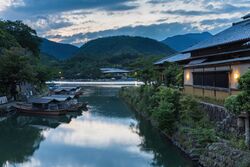 Katsura River bank with pleasure boats and illuminated building at sunset Kyoto Japan.jpg