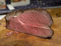 Joint of roast beef on a wooden board, cooked medium rare and carved.
