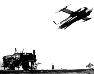 a black and white film photo of a large unmanned drone being launched near an old vehicle