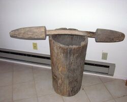 A large wooden mortar with a wooden pestle lying horizontally across the top.