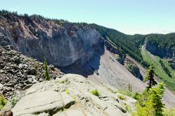 Wall of rock covered with trees and rubble extending down its side.