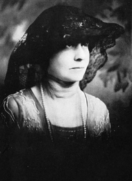 Black-and-white headshot of a woman wearing a hat draped with lace
