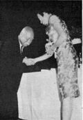 Whang-Peng is wearing a traditional dress and is standing and shaking the hand of Wang Yun-wu.