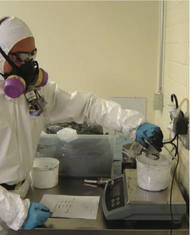 A man wearing a white lab coat reaches over a beaker containing white powder on a balance