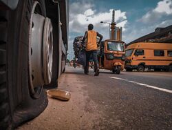 A broken down truck, A cart pusher, A tricycle and a bus in Lagos.jpg