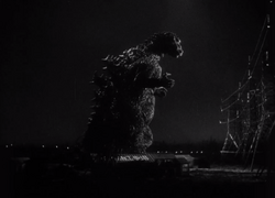 Dark night scene with city lights in the background, with a massive dinosaur-like creature stands on hind legs facing tall electrical towers