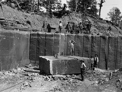 Workers standing in a quarry with a large stone block.
