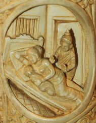 Ivory tusk showing a woman and a child sleeping on a bed, and a man standing besides the bed.