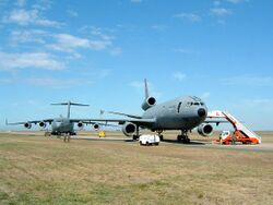 Two large gray jet aircraft on roomy ramp surrounded by grass, both angled away from the runway. The one closer to camera is three-engined, while the one further in the background is four-engined.