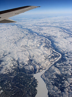 An aerial photo viewing down to earth with rivers visible. Ground is covered by snow, with trees in the lower left and in the valleys of the rivers.