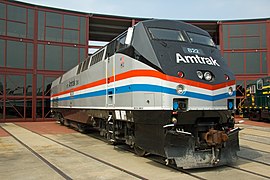 A gray diesel locomotive with a black cab area. Red, white, and blue stripes run along the sides and wrap across the front, where they pinch slightly