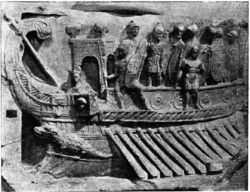 A galley with its oars out equipped with a small tower-like structure and a group of battle-ready Roman legionnaires standing on the upper deck