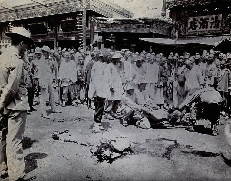 File:Man being beheaded in China, while the body of a man already executed lays in the street with three westerners in the crowd.jpg