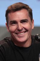 A 44-year-old man with short, brown hair, talking into a microphone, and smiling to the right of the camera.