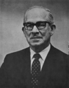 A photographic portrait of a man wearing glasses and a suit