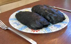 Two black loaves sit on a plate with knife and fork beside them.