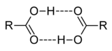 This image illustrates how two carboxylic acids, C O O H, can associate through mutual hydrogen bonds. The hydroxyl portion O H of each molecule forms a hydrogen bond to the carbonyl portion C O of the other.