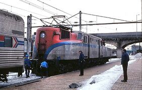 A gray electric locomotive with red ends and a blue side stripe