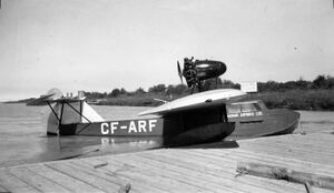photo of single engine flying boat in the water, tied up at a wharf.