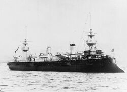 A large, black ship at anchor; the vessel has two wide, squat masts with bulky platforms for light guns.