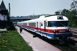 A white passenger trainset with red and blue horizontal stripes on the side