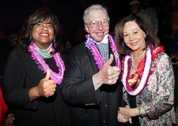 Three people are smiling with Hawaiian leis around their necks.