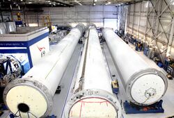 Long, cylindrical rocket sections lie in a warehouse