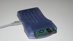 Photo of a blue colored device with a large slot in front, and a cable is attached to the device